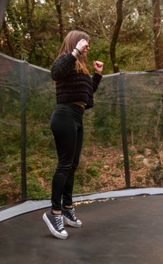 Dağlarda trambolinde zıplayan çocukluğunu anımsatan siyah giyinmiş genç bir kadın..