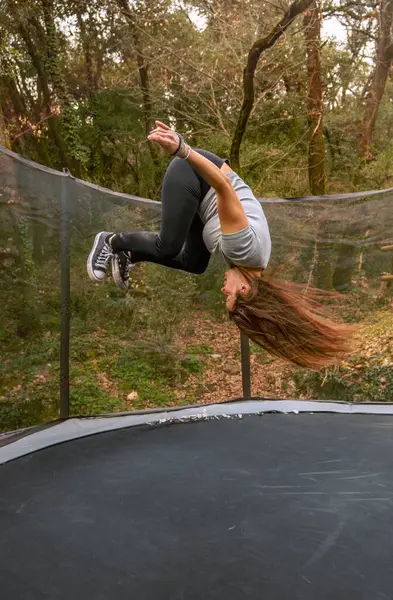 Spor giyinmiş genç bir kadın trambolinde ters takla atıyor.
