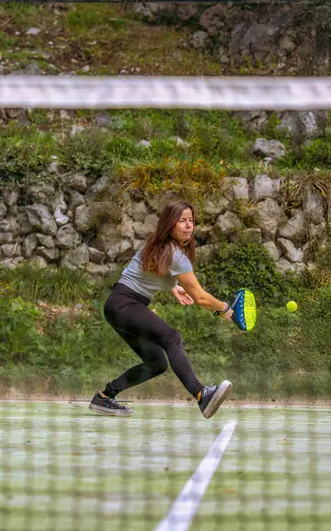 Genç ve formda bir sporcunun, dışarıda bir sahada topun Padel oynamasını beklerken raketiyle ters vuruş yapacak pozisyonda olması..