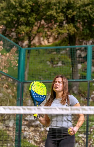 Güçlü genç bir atlet topu servis etmek üzere açık bir dağ kortunda ağın yanında Padel oynamak için..