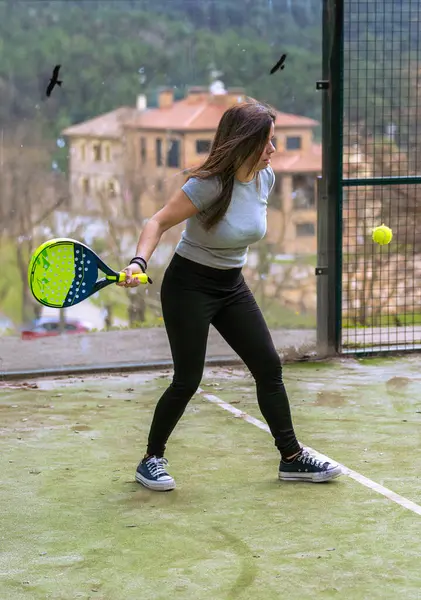 Genç adam topu izliyor, raketiyle dağlardaki açık bir padel kortunda vurmaya hazır..