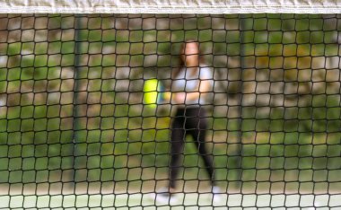 Padel net net net bir odak ve arka planda topu bulanık bekleyen bir padel oynatıcı.