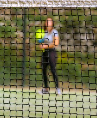 Padel net net net bir odak ve arka planda topu bulanık bekleyen bir padel oynatıcı.