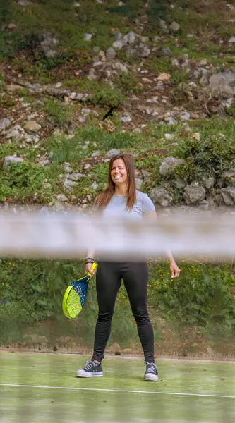 Padel kortunun arkasında mutlu, gülümseyen genç bir kadın. Maçın başında durup poz veriyor..