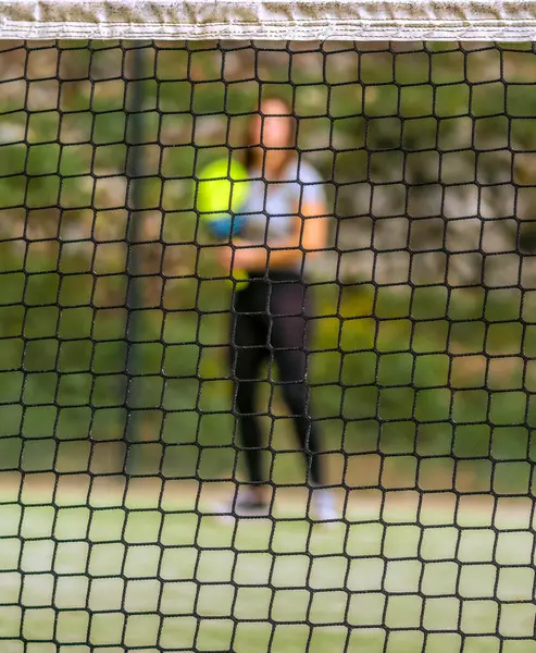Padel net net net bir odak ve arka planda topu bulanık bekleyen bir padel oynatıcı.