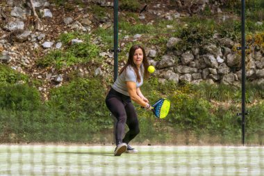 Genç, atletik, kaslı, Padel oynayan bir kadının bir ağ üzerinden top ters vuruş için ona doğru gelirken izlediği bir görüntü..