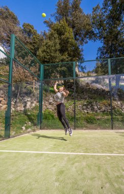 Genç, güçlü, atletik bir kadın, mutlu bir şekilde gülümsüyor, dağlarda bir raket maçında topa vurmak için zıplıyor..