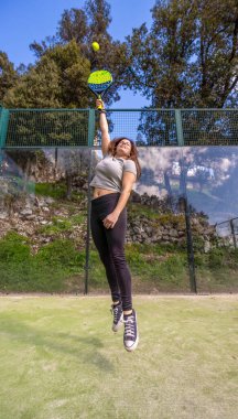 Güçlü, genç bir atlet koluyla atlayıp raketiyle dışarıda bir dağ kortunda raketlere vuruyor..