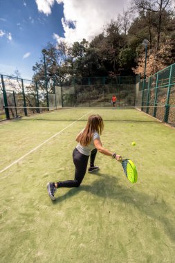 Genç bir ırklar arası çift, bir Katalan köyünün kırsal kesimindeki açık bir sahada Padel top oynarken, Padel topu bir forehand ile geri dönüyor..