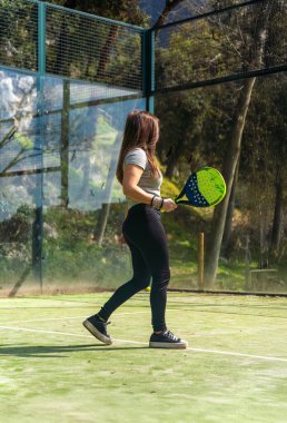 Padel oynayan genç, güçlü bir atlet, oynamadan önce yönünü bulmak için açık yeşil bir sahada yürüyor..