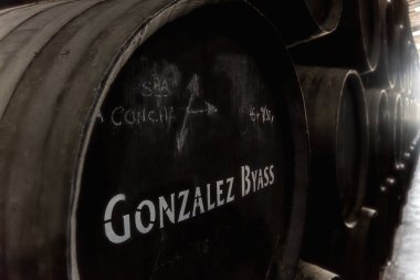 Yakından bakınca, fıçının üzerinde Gonzalez Byass Tio Pepe damgası olan geleneksel bir şaraphanede muhafaza etmek için kullanılan ahşap şarap fıçılarının az ışık alan görüntüsü..