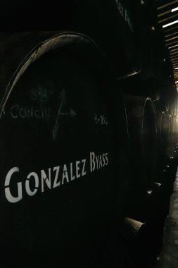 Yakın çekim, ahşap şarap fıçılarının düşük ışık manzarası geleneksel bir şaraphanede muhafaza edilmek üzere Gonzalez Byass Tio Pepe markası beyaz harflerle işaretlenmiş..