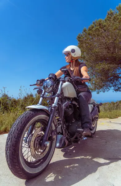 Klasik bir motosikletli kadın güneşli bir günde manzaraya bakıyor..