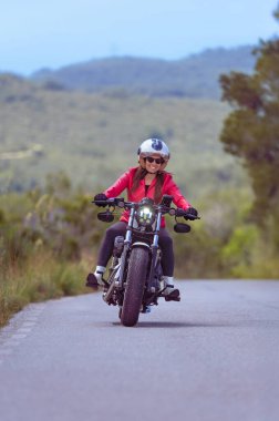 Güzel, mutlu, gülümseyen bir kadın motosikletlinin Harley-Davidson Sporcusu 'nun virajına eğilmiş bir şekilde dolambaçlı bir sahil yolunda sürüşünün ön görüntüsü..