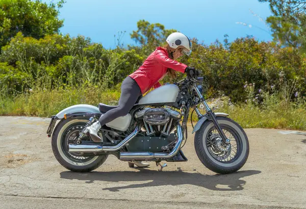 Harley Davidson spor motosikletine binmek için gidona yaslanmış kırmızı deri ceket giyen genç bir motorcu..