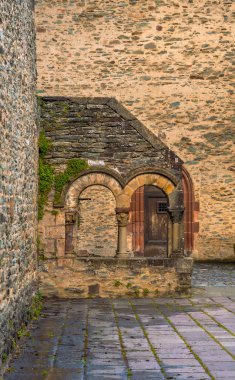 Ortaçağ taş kemerlerinin arkasında antik taş bir duvar ve Fransa 'daki Sainte-Foy Manastırı Kilisesi' nin dışında demir parmaklıklı ahşap bir kapı var..