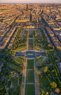 Güneş batarken Champ de Mars ve Ecole Militaire 'in gökyüzü manzarası Paris' teki binaların çatılarını aydınlatan altın ışıkla, Eyfel Kulesi 'nin gölgesi çatıya yansıtılıyor.