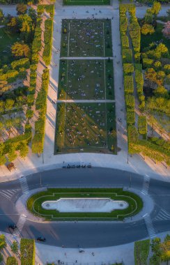 Ailelerin, çiftlerin ve dostların rahatlama, piknik yapma ve gün batımında Champ de Mars 'ın çimlerinde Eyfel Kulesi' nin fotoğraflarını çekme görüntüsü..