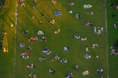Paris Champ de Mars parkının çimlerinde dinlenen ve piknik yapan birkaç insanın hava görüntüsü. Gün batımının son ışığı altın saatinde..