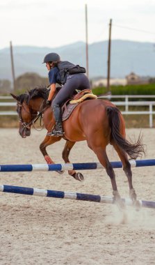 Genç bir kadın binicinin, kum binicisi arenasında bir engelin üzerinden atlarken mükemmel bir konumda ata binişinin arka görüntüsü..