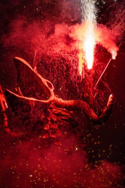 Şeytani yaratık boynuzlarında havai fişeklerle çığlık atıyor. Etrafında duman ağları, ateş kıvılcımları ve açık hava festivalinde kızılımsı renkte barut var..