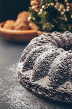 Pudra şekerli çikolatalı bisküviler. Fındıklı kek, kuru üzüm ve kuru meyve. Xmas için pişirme. Noel desenli şenlikli kek. Masada koniler ve baharatlar.