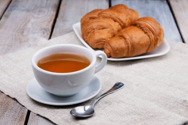 Çay ve kruvasanla kahvaltı. Yeni pişmiş kruvasan. Kruvasan üretimi kavramı. Taze tereyağlı kruvasan. Fransız ve Amerikan kruvasanları ve fırınlanmış hamur işleri dünya çapında sevilir..
