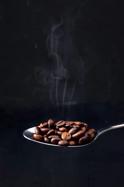 コーヒー豆の背景 暗い背景にローストコーヒー豆 コーヒーコンセプト モックアップクローズアップ スプーンには焙煎したコーヒー豆がたくさん入っています — ストック写真