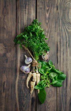 Parsley, garlic, basil on a wooden background. Top view. Flat lay. A bunch of parsley with roots. Ingredient for vegetable soup. Vegetarianism. Useful product. healthy eating. copy space.