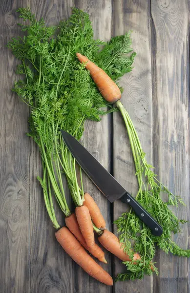 Cut ripe raw orange carrot  on kitchen wooden board. Sliced carrot with knife. Flat lay view. Layout of fresh vegetables and flavorings. Prepare ingredients for cooking. Healthy food.
