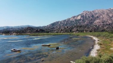 Tekneler ve dağlar göl kıyısında görülebilir. Gölün dibi yosunlu. Kamera yana hareket ediyor..