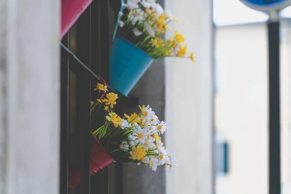 Colorful flowers hanging on the window with a metal bucket-shaped vase