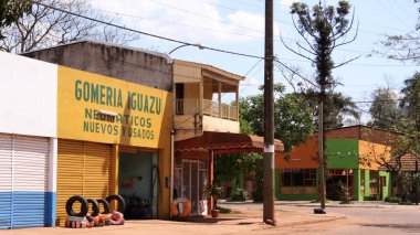 Iguazu 'da sakin bir caddede lastik ve hizmet gösteren renkli dükkanlar yer alıyor. Güneş ışığı binaları aydınlatıyor ve bu mahallede canlı bir atmosfer yaratıyor..