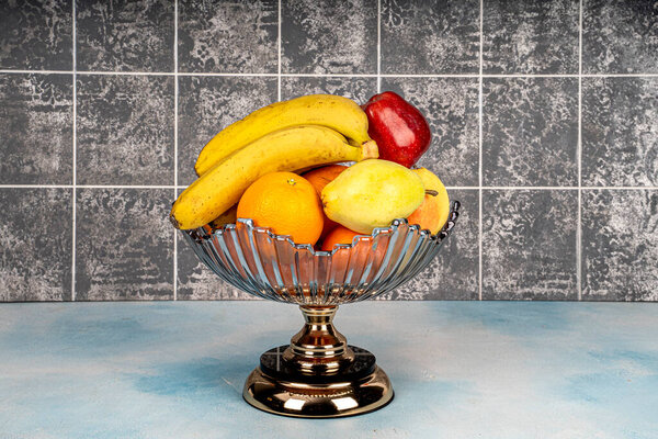 Разнообразие спелых фруктов в стильной стеклянной чаше на деревянном столе, украшения дома