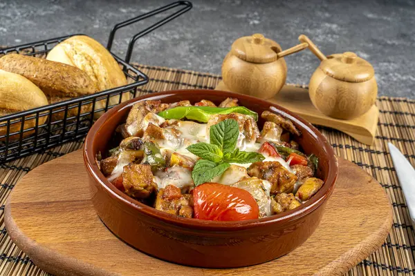 Ekmek ve sebzeyle servis edilen kil güveçte sotelenmiş tavuk.
