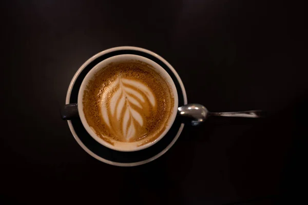 带有牛奶图案和泡沫的新鲜咖啡 卡布奇诺在黑暗桌上的瓷杯里高质量的照片 — 图库照片