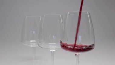 Kırmızı şarap. Şarap beyaz arka planda bir bardağa dökülüyor. Yakın plan çekim. Şişeden kadehe yavaş yavaş kırmızı şarap dökme hareketi. Yüksek kalite 4k görüntü