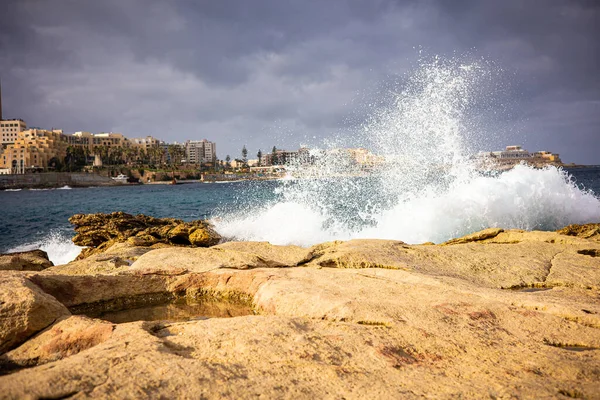 A lot of spray from the waves of the ocean against the backdrop of the buildings of the city of Valletta. Coast of the island of Malta in winter. High quality photo