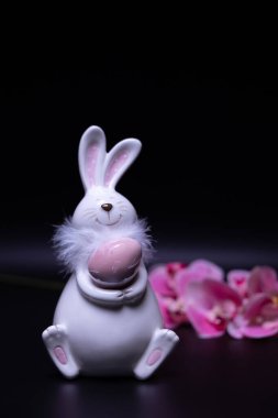 Porcelain toy rabbit, Easter decoration on a black background. Pink orchid flowers. High quality photo