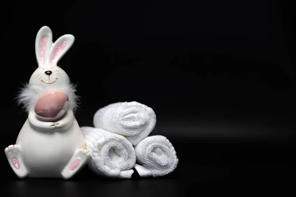 Easter white bunny with a brown egg on a black background with white spa towels. Easter preparation. High quality photo
