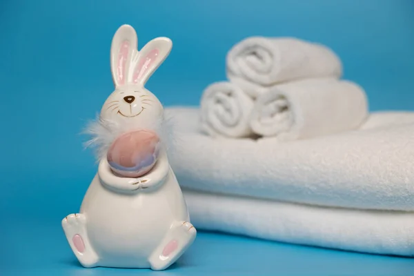 Easter white bunny with brown egg blue background and white towels. Easter preparation. High quality photo