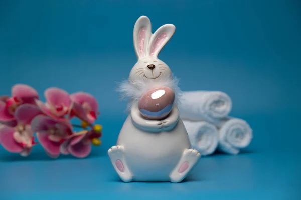 Easter white bunny with brown egg blue background and white towels. Easter preparation. High quality photo