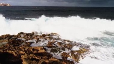 Beyaz büyük dalgalar Malta adasının taş kıyılarını yıkıyor. Bir İHA 'dan ateş etmek. Yüksek kaliteli FullHD görüntüler