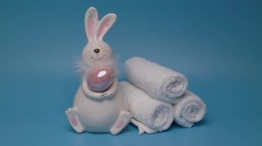 Easter white bunny with brown egg blue background and white towels. Easter preparation. High quality 4k footage