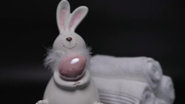 Easter white bunny with brown egg black background and white towels. Easter preparation. High quality 4k footage