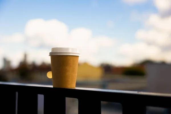 A paper cup for coffee with a white lid stands on the railing on a sunny summer day. High quality photo