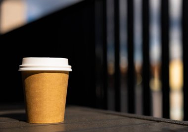 Beyaz kapaklı bir kağıt kahve fincanı güneşli yaz gününün dışında siyah masanın üzerinde duruyor. Yüksek kalite fotoğraf