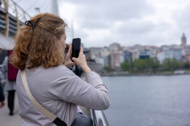 Dişi turist manzaranın fotoğrafını çeker. Kız telefonuyla yarım bir dönüş yapıyor, fotoğraf çekiyor. Yüksek kalite fotoğraf