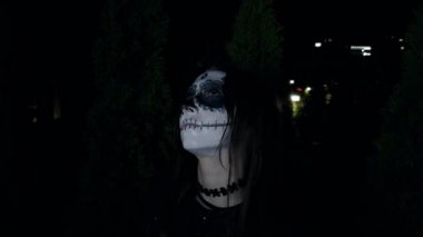Kafatası şekeri yüzlü bir kız kafasını çevirir ve dikkatlice kameraya bakar. Tüm azizler için kavram. Yüksek kalite 4k görüntü