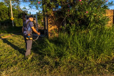 Marilia, Sao Paulo, Brezilya, 22 Mart 2023. İşçi, manuel benzin fırça kesicisiyle Marilia 'nın kırsal kesimindeki bir çiftliğin kapısındaki yağmurla birlikte büyüyen otları kesiyor.